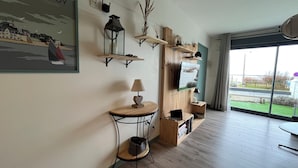 A modern living room with a wooden floor, a mounted TV, and a large window offering a view of the outdoors. - Bélicine, seafront apartment for 5 people  (LE CROTOY)