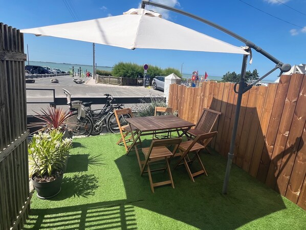 A patio with a table and chairs, a wooden fence, and a view of the sea. - Bélicine, Ocean View Apartment for 5 People (LE CROTOY)