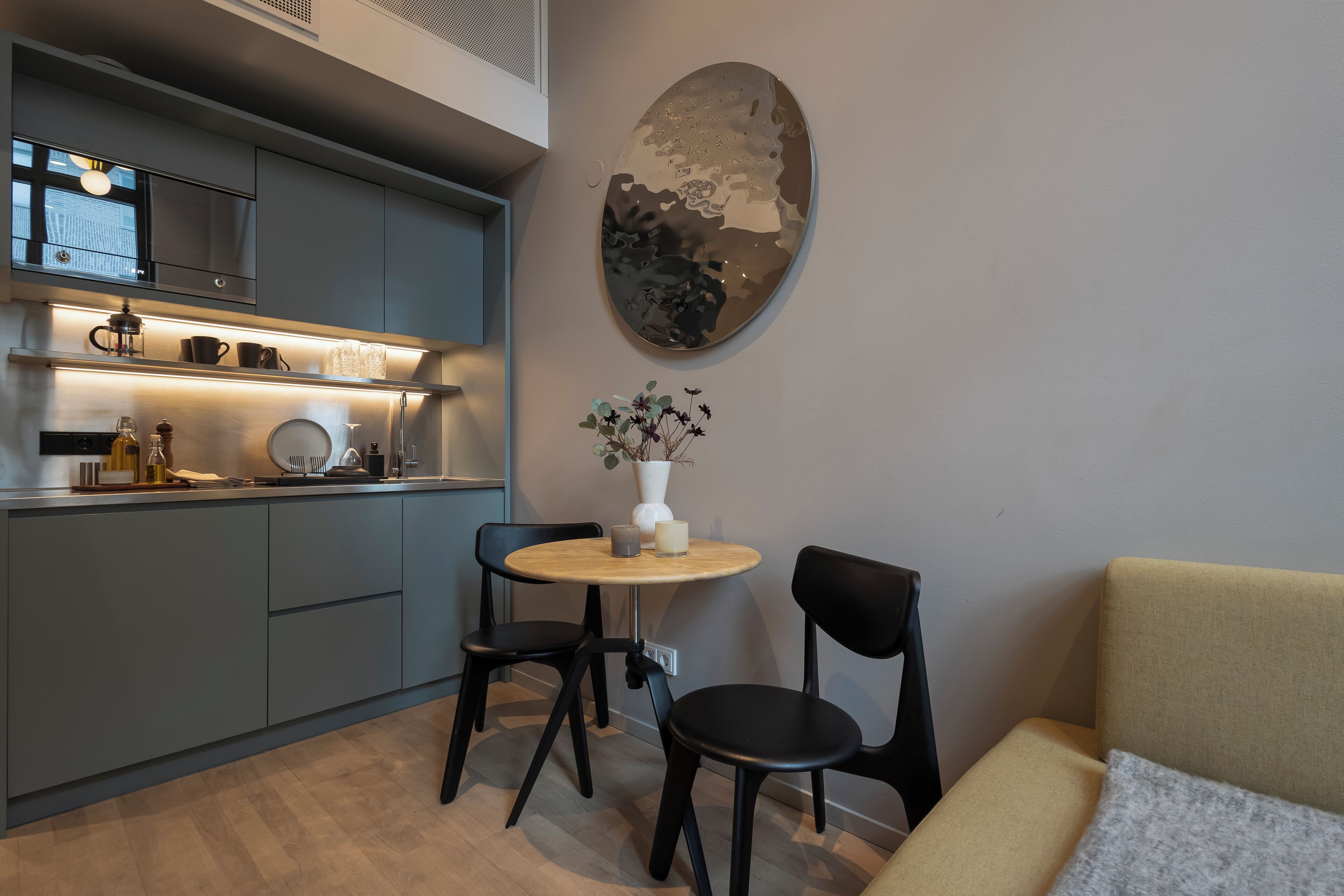 Una cocina moderna con armarios grises, una mesa redonda con dos sillas y un adorno en la pared.