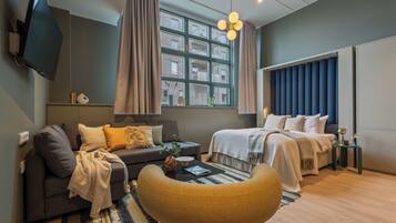 Een moderne hotelkamer met een bank, een bed, een televisie en een groot raam met gordijnen.