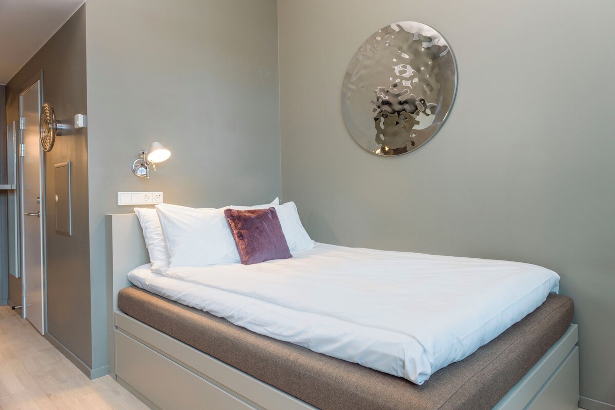 A modern bedroom with a bed, a wall-mounted light, and a decorative mirror.
