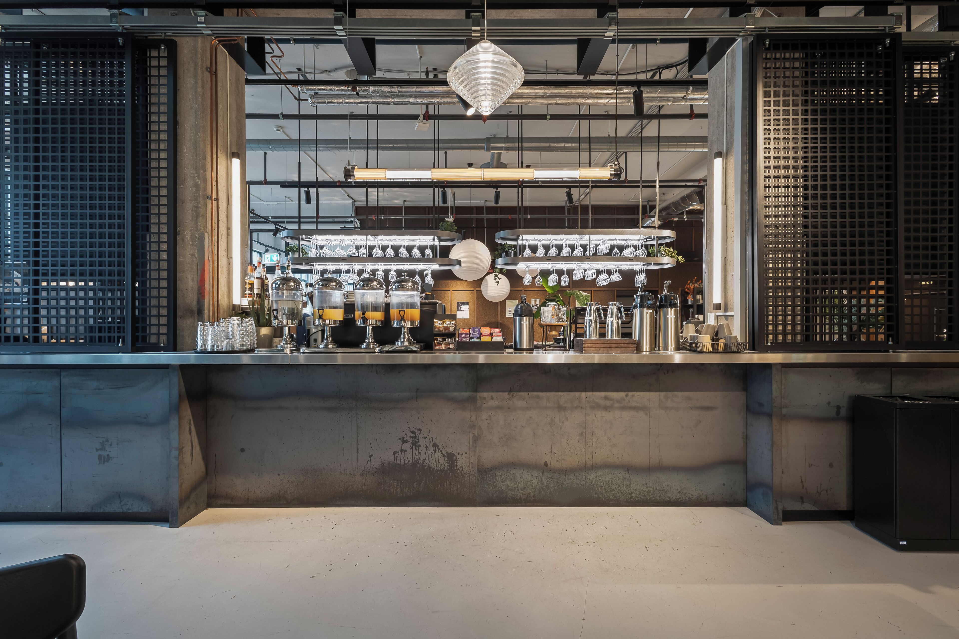 Een moderne keuken met roestvrijstalen apparatuur, een beton aanrechtblad en hangende pendelverlichting.