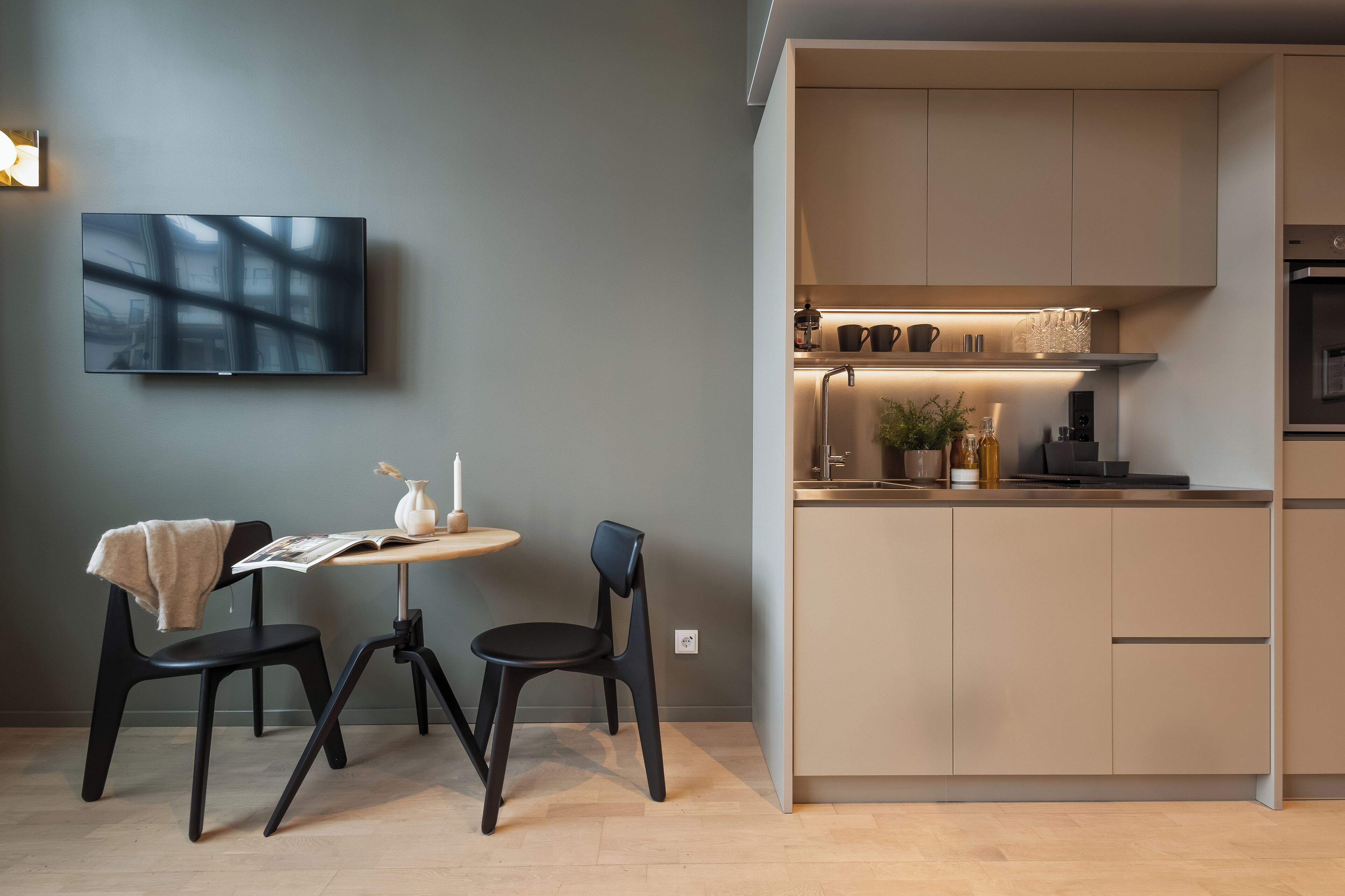 A modern kitchen with a built-in stove, a dining area with two chairs and a table, and a flat-screen TV mounted on the wall.