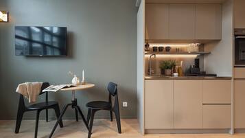 A modern kitchen with a built-in stove, a dining area with two chairs and a table, and a flat-screen TV mounted on the wall.
