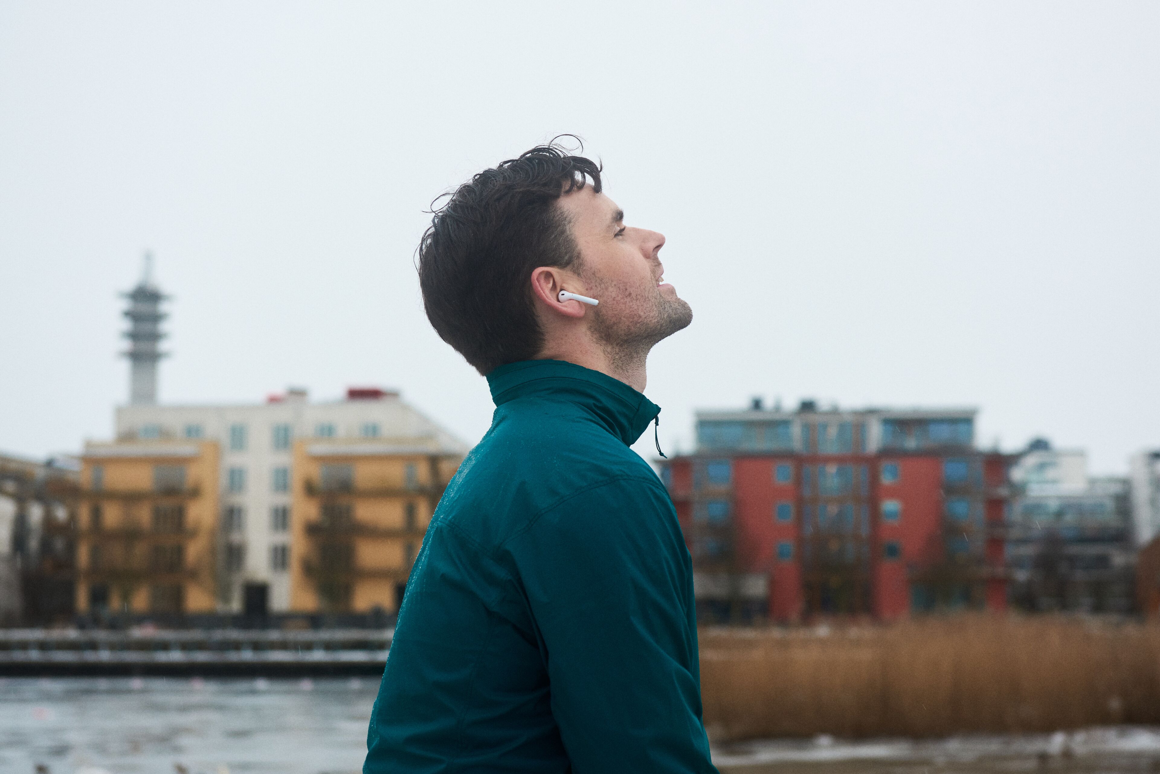 Une personne portant une veste turquoise, debout devant un paysage urbain.