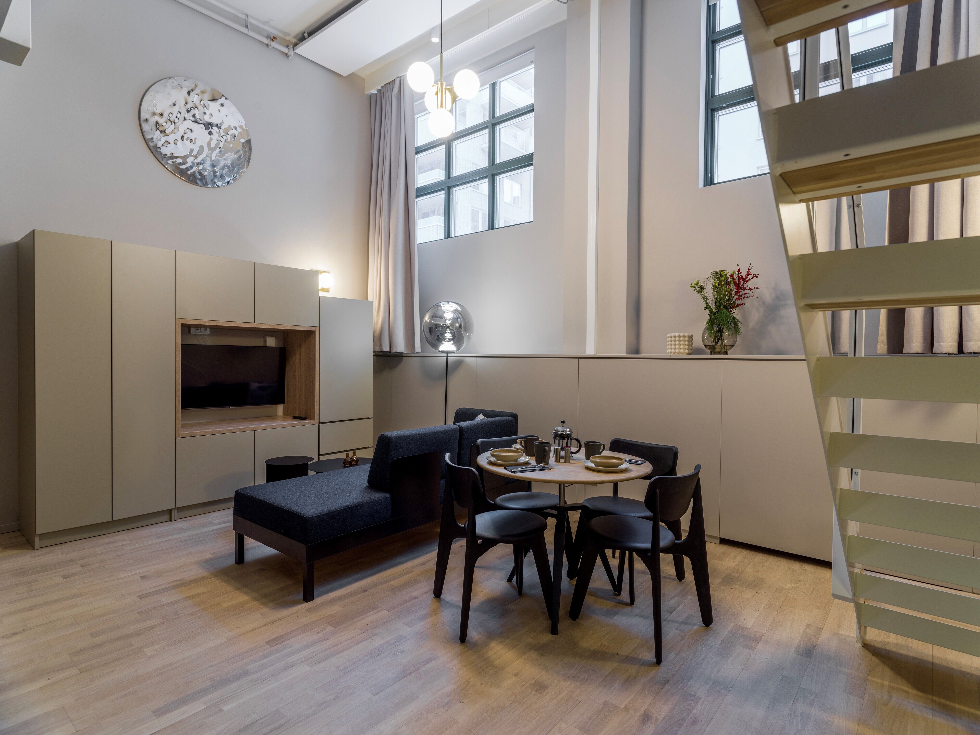 A modern living room with a sofa, dining table, and chairs, a flat-screen TV, and a large window with curtains.