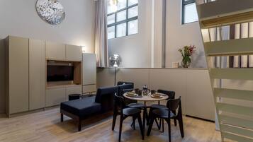 A modern living room with a sofa, dining table, and chairs, a flat-screen TV, and a large window with curtains.