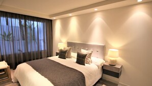 Een moderne slaapkamer met een groot bed, twee bedlampen en uitzicht door dunne gordijnen.