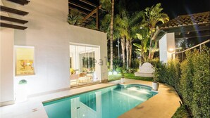 Een modern huis met een zwembad, een terras en weelderige begroeiing.