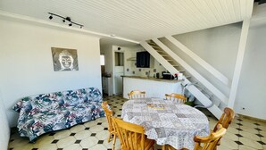 En matplats med ett bord och stolar, en mönstrad soffa och ett kök i bakgrunden.