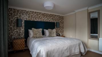 A bedroom with a large bed, two bedside tables, a headboard, and patterned wallpaper.