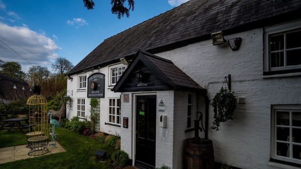A white building with a black roof, a sign reading "The Brewers Inn," and a small garden area with a birdcage and a wooden barrel. - The Brewers Inn (Cambridge)
