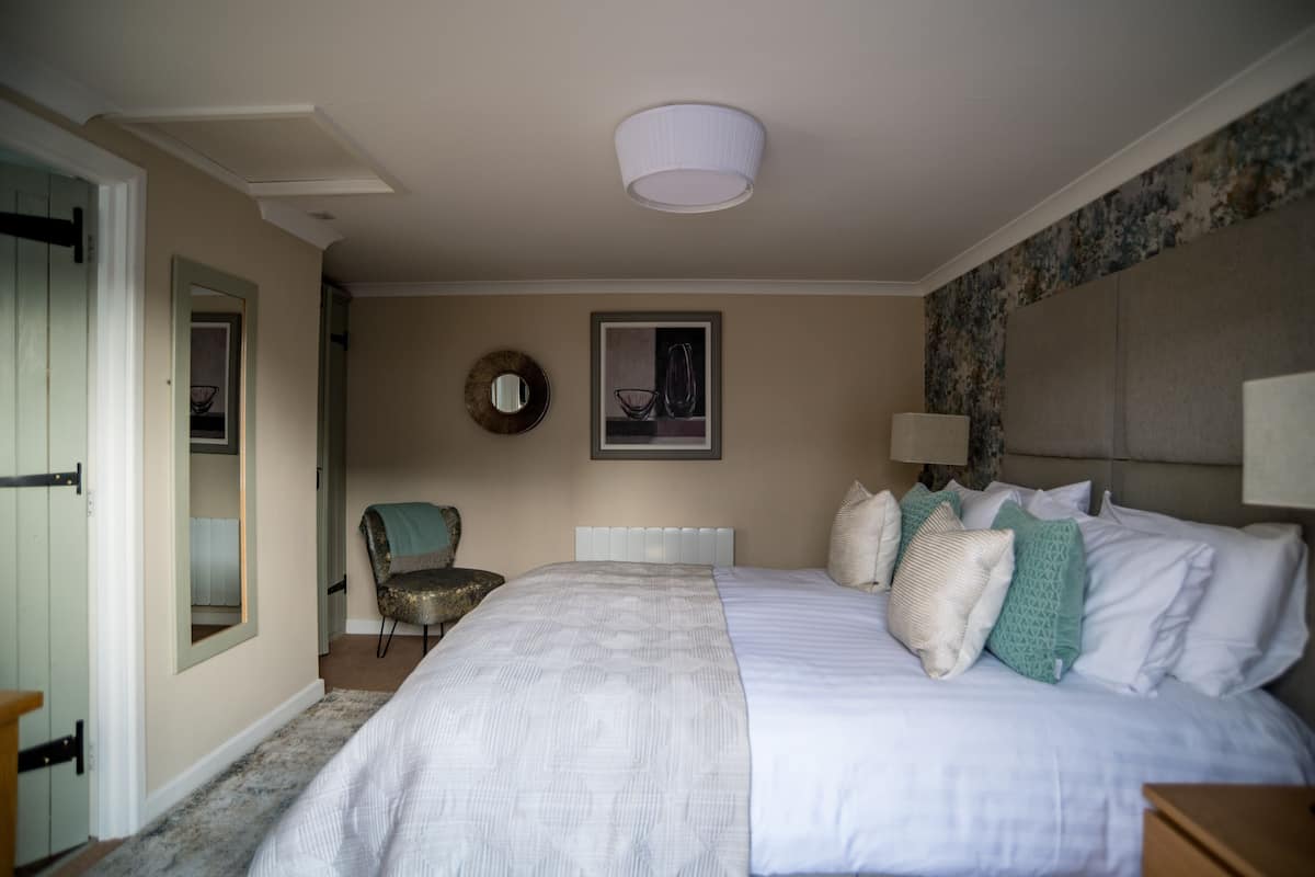 A bedroom with a large bed, a chair, a bedside table, a lamp, and a framed picture on the wall.