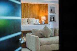 A hotel room with a bed, a bedside table with a lamp, a sofa, and a wooden panel wall. - Paradise Beach Villa Santa Pila (San Miguel de Cozumel)