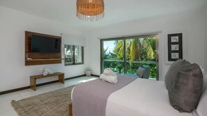 A modern bedroom with a large bed, a television mounted on the wall, a bench, and a view of the outdoors. - Paradise Beach Villa Santa Pila (San Miguel de Cozumel)