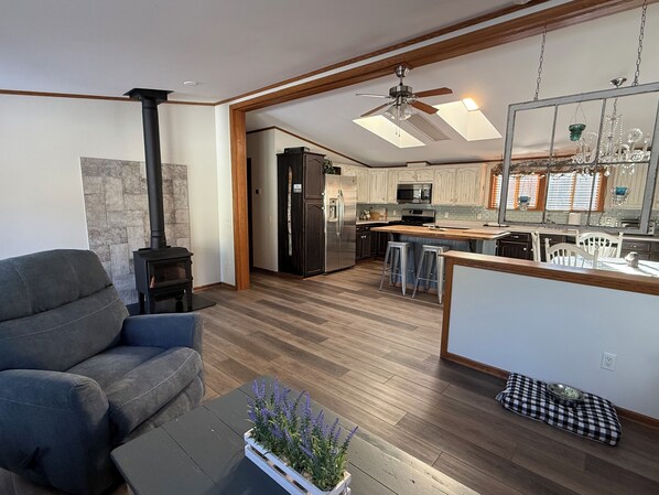 A modern living room with a sofa, a coffee table with a plant, a fireplace, and a kitchen with wooden cabinets and a large island.
