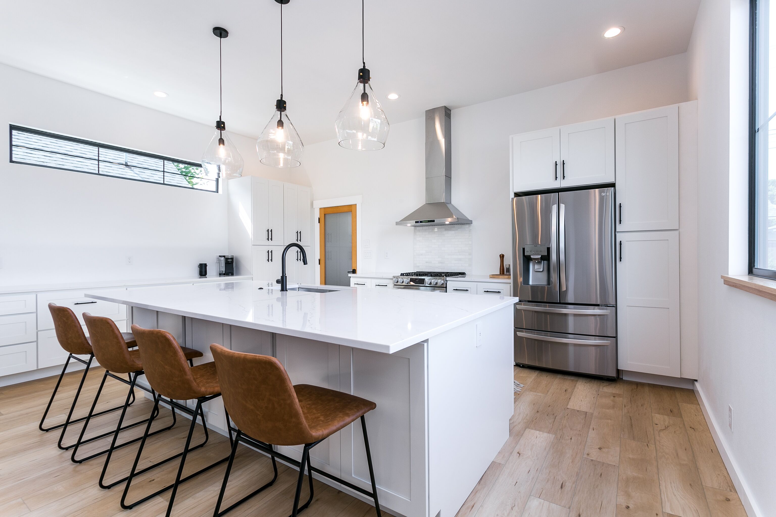 Une cuisine moderne dotée d’un grand îlot central, d’appareils électroménagers en acier inoxydable et de luminaires suspendus.