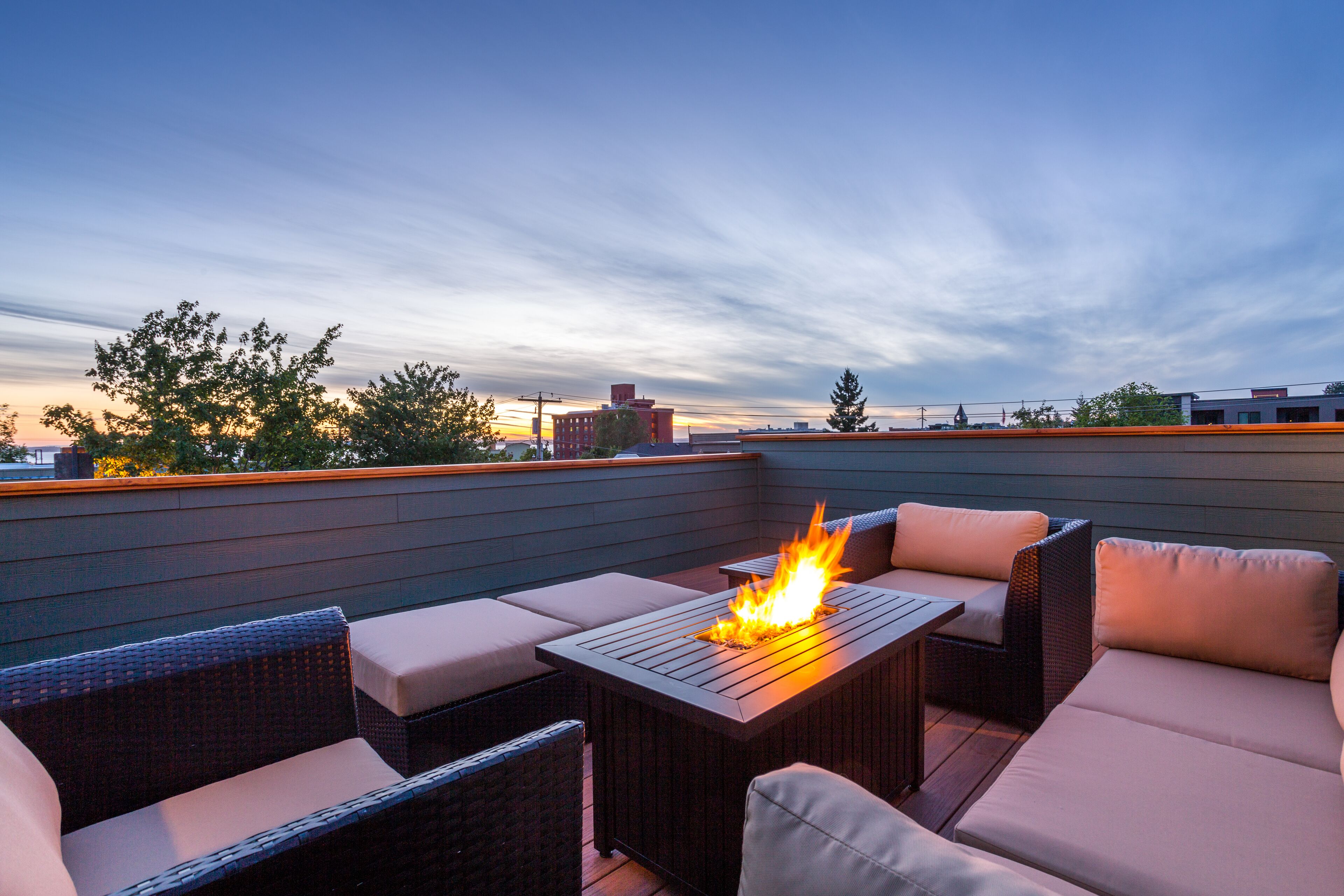 A rooftop patio with a fire feature, wicker furniture, and a view of the city skyline.