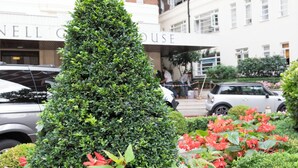 Un edificio con fachada de ladrillo, una estatua y un jardín bien cuidado con flores rojas y un seto recortado.