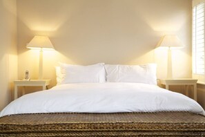 A bed with white linens, two bedside tables with lamps, and a woven rug. - Art Deco Studio on 6th Floor, Chelsea (London)