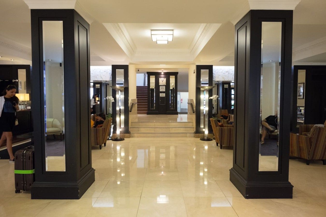 Un hall d’hôtel doté d’un sol ciré, d’un comptoir d’accueil, de coins salon et d’un escalier menant à un autre niveau.
