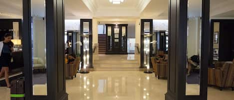 A hotel lobby with a polished floor, a reception desk, seating areas, and a staircase leading to another level.