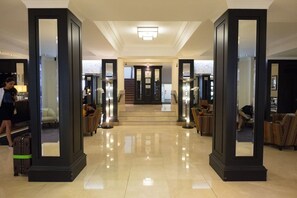 Et hotel lobby med skinnende gulv, en reception, siddeområder og en trappe til et andet niveau.