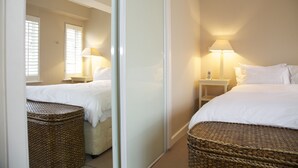 Un dormitorio con una cama, mesitas de noche, una lámpara, una cesta de mimbre y un espejo.