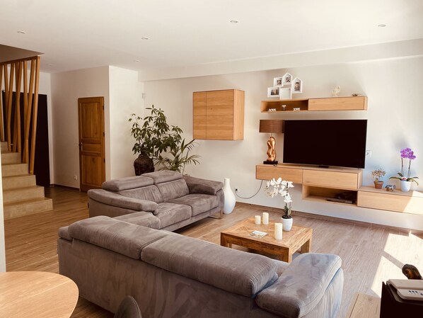 Uma sala de estar moderna com sofá em forma de L, televisão e mesa de centro de madeira.