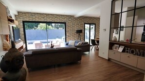 A modern living room with a sofa, a Buddha statue, and a large window overlooking a backyard. - Maison Paisible (VEDENE)