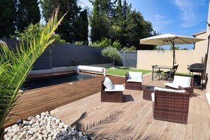 Um pátio externo com mobiliário de vime, piscina e área de churrasco.