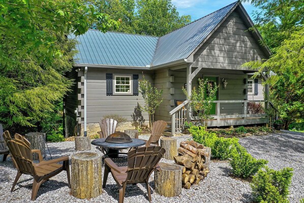A house with a covered patio area featuring Adirondack chairs and a fire pit. - Cozy log cabin with rustic decor & hot-tub to enjoy! (Townsend)