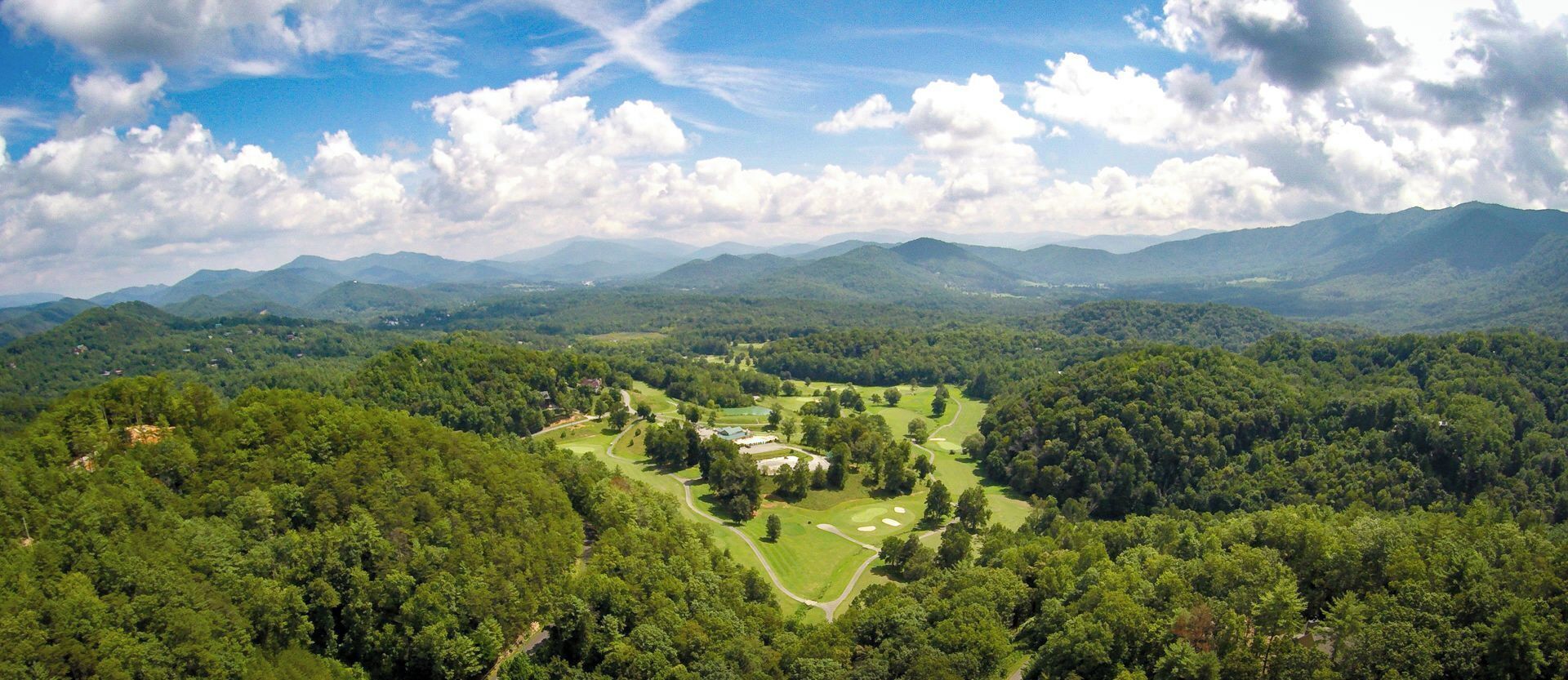 A golf course surrounded by dense forest and mountains.