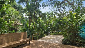 A wooden deck with a bench, surrounded by lush greenery and a clear blue sky. - Tranquil Vero Beach Home – Private Pool + Special Booking Discounts! (Vero Beach)