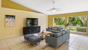 A living room with a sofa, ottoman, coffee table, TV, and a ceiling fan. - Tranquil Vero Beach Home – Private Pool + Special Booking Discounts! (Vero Beach)