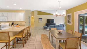 A modern kitchen with white cabinets, a central island with seating, and a dining area with a wooden table and chairs. - Tranquil Vero Beach Home – Private Pool + Special Booking Discounts! (Vero Beach)