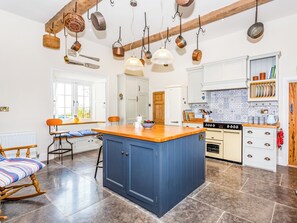 Cocina con isla central, vigas de madera, ollas colgantes y ventana con vistas.