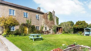 Un bâtiment en pierre avec une cour verdoyante, une table de pique-nique et un parterre de fleurs.