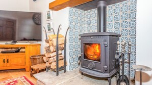 Un salon chaleureux avec un poêle à bois, une télévision et un mur recouvert de carreaux décoratifs.