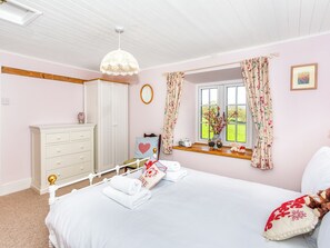 A bedroom with a bed, a dresser, a mirror, a window with curtains, and a hanging light fixture.