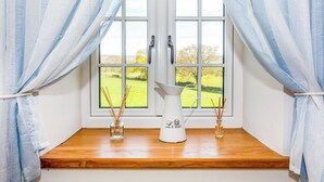 A window with two white curtains, a wooden ledge, and two glass vases with reed sticks. - The Farmhouse - UK33419 (West Witton, near Leyburn)