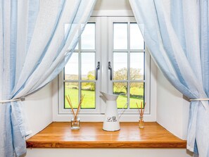 Una ventana con dos cortinas blancas, un alféizar de madera y dos jarrones de vidrio con ramas de caña.