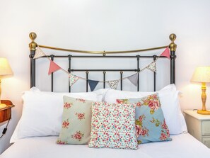 Una cama bien hecha con almohadillas estampadas con motivos florales y cabecera de metal.