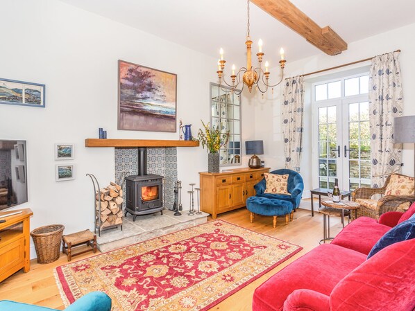 A cozy living room with a fireplace, a blue armchair, a red sofa, and a chandelier. - The Farmhouse - UK33419 (West Witton, near Leyburn)