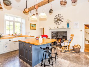 A spacious kitchen with a large island, wooden bar stools, a fireplace, and hanging kitchen utensils.
