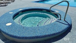 Una bañera de hidromasaje con una piscina al fondo, rodeada de sillones de descanso y una cerca blanca.