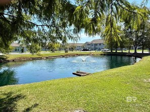 Un étang paisible avec une fontaine, entouré de pelouses et d’arbres bien entretenus, avec des bâtiments en arrière-plan.