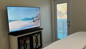 Un dormitorio con cama, televisor sobre un mueble, ventilador de techo y puerta con vistas.