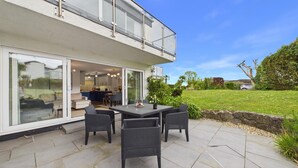 A modern house with a patio, a dining area, and a kitchen visible through glass doors.