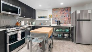 A modern kitchen with stainless steel appliances, a microwave, oven, and a refrigerator. There is a wooden cutting board on the counter and a dish rack with utensils. - Artistic Craftsman Style Home Downstairs Apartment (Portland)